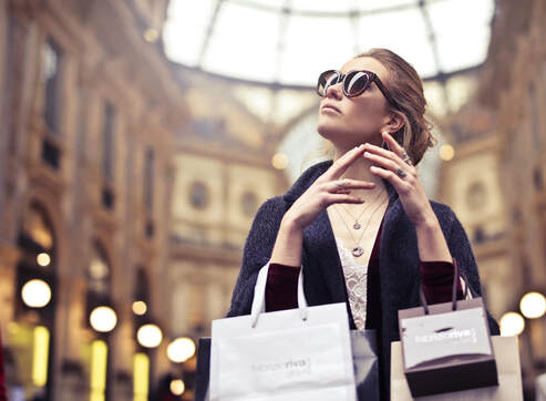 Woman wearing sunglasses and with shopping bags hanging from arms looking up in the Galleria of Milan